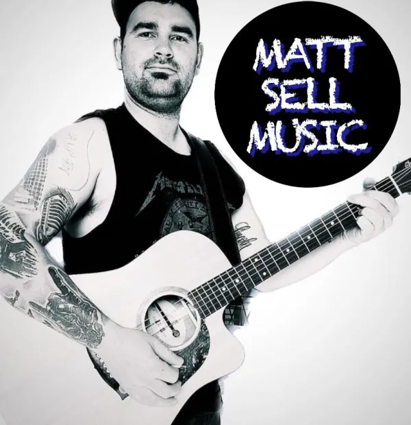 A man with dark hair and tattoos holding a guitar